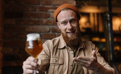 Adobe Stock Man holding glass of beer at a distance, smiling at it. Adobe stock